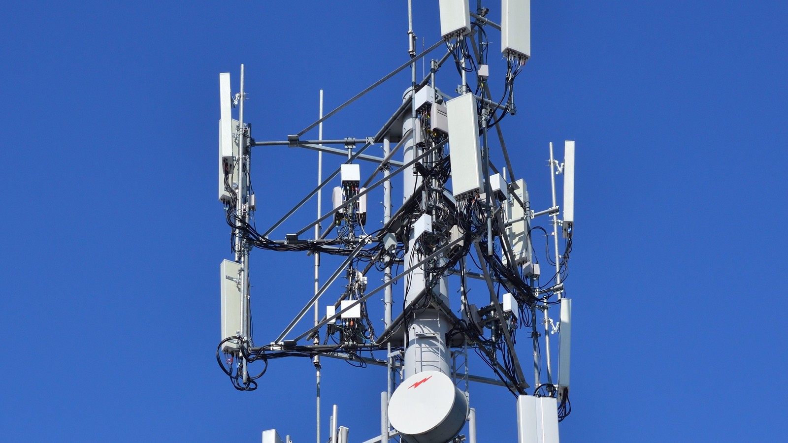 Close-up engineering view of telecommunications Massive MIMO antenna array hardware on cellular base station with microwave dish and high-speed feeder lines