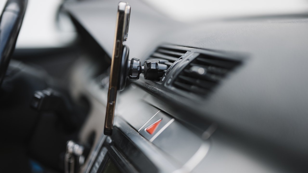 Smartphone mounted on modern vehicle dashboard air vent fast charging during navigation
